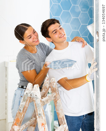 Couple in the bathroom glues ceramic tiles on the wall Couple in the bathroom glues ceramic tiles on the wall 134054697