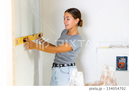 Woman measures deviations from predetermined vertical wall using building level Woman measures deviations from predetermined vertical wall using building level 134054702