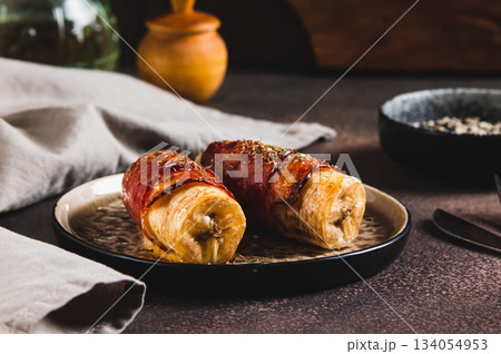 Baked banana roll with bacon on a plate on the table Baked banana roll with bacon on a plate on the table 134054953