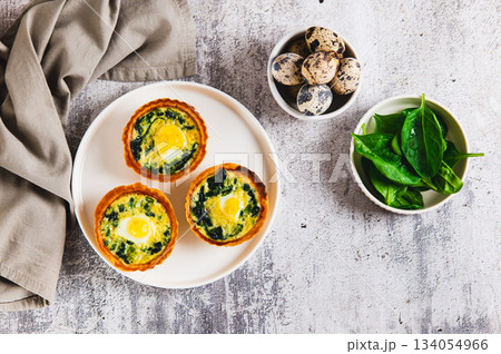 Baked tartlets with quail eggs and fresh spinach on a plate on the table top view Baked tartlets with quail eggs and fresh spinach on a plate on the table top view 134054966