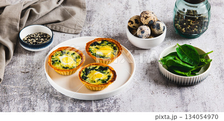 Baked tartlets with quail eggs and fresh spinach on a plate on the table web banner 134054970
