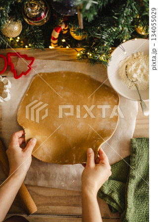 Holiday background. Rolling pin, female hands and raw rolled dough, cooking Christmas gingerbread cookies. Top view Holiday background. Rolling pin, female hands and raw rolled dough, cooking Christmas gingerbread cookies. Top view 134055029