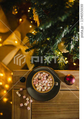 Holiday, Christmas background. A cup with hot chocolate and marshmallows on the table with Christmas tree on background Holiday, Christmas background. A cup with hot chocolate and marshmallows on the table with Christmas tree on background 134055030