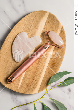 Rose quartz gua sha tool and face massage roller on wooden tray, beauty abstract photo. Top view 134055080