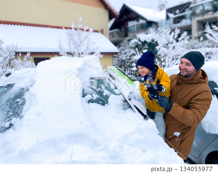 Father and son clear snow from a car in a winter neighborhood during a sunny morning Father and son clear snow from a car in a winter neighborhood during a sunny morning 134055977