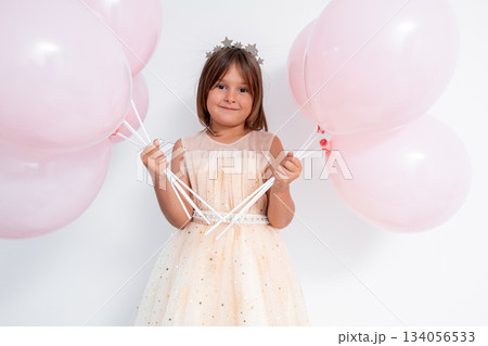 Young caucasian girl in party dress with pink balloons and tiara 134056533