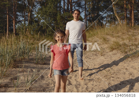 Father and daughter walk one after other along beach sand near forest in summer, lifestyle 134056818