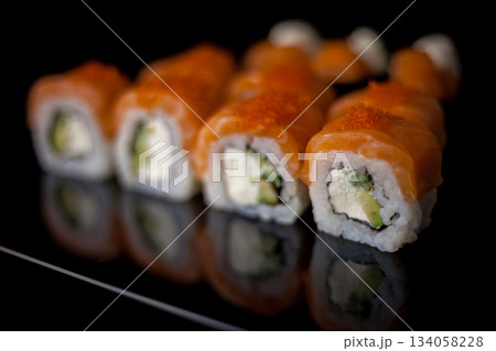 Salmon sushi set. Sushi roll Philadelphia with red fish, salmon, red caviar. Roll with soft avocado and cream cheese under a layer of massago caviar. Classic sushi on a black background. Food. 134058228
