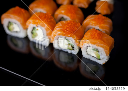Salmon sushi set. Sushi roll Philadelphia with red fish, salmon, red caviar. Roll with soft avocado and cream cheese under a layer of massago caviar. Classic sushi on a black background. Food. Salmon sushi set. Sushi roll Philadelphia with red fish, salmon, red caviar. Roll with soft avocado and cream cheese under a layer of massago caviar. Classic sushi on a black background. Food. 134058229