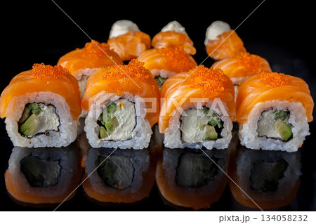 Salmon sushi set. Sushi roll Philadelphia with red fish, salmon, red caviar. Roll with soft avocado and cream cheese under a layer of massago caviar. Classic sushi on a black background. Food. Salmon sushi set. Sushi roll Philadelphia with red fish, salmon, red caviar. Roll with soft avocado and cream cheese under a layer of massago caviar. Classic sushi on a black background. Food. 134058232