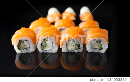 Salmon sushi set. Sushi roll Philadelphia with red fish, salmon, red caviar. Roll with soft avocado and cream cheese under a layer of massago caviar. Classic sushi on a black background. Food. Salmon sushi set. Sushi roll Philadelphia with red fish, salmon, red caviar. Roll with soft avocado and cream cheese under a layer of massago caviar. Classic sushi on a black background. Food. 134058233