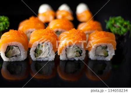 Salmon sushi set. Sushi roll Philadelphia with red fish, salmon, red caviar. Roll with soft avocado and cream cheese under a layer of massago caviar. Classic sushi on a black background. Food. Salmon sushi set. Sushi roll Philadelphia with red fish, salmon, red caviar. Roll with soft avocado and cream cheese under a layer of massago caviar. Classic sushi on a black background. Food. 134058234