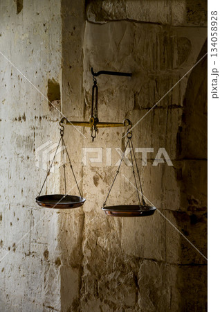 Antique metal scales hang in the darkness on an old, damaged stone wall. Color vertical photo. Antique metal scales hang in the darkness on an old, damaged stone wall. Color vertical photo. 134058928