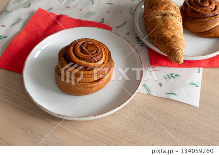 Cinnamon roll and freshly baked pastries on cozy table setting. Christmas mood Cinnamon roll and freshly baked pastries on cozy table setting. Christmas mood 134059260