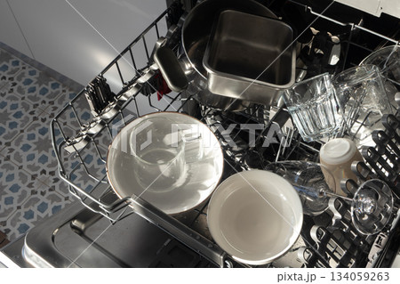 Open dishwasher with clean dishes in morning sunlight. Cleaning routines, sustainable living 134059263