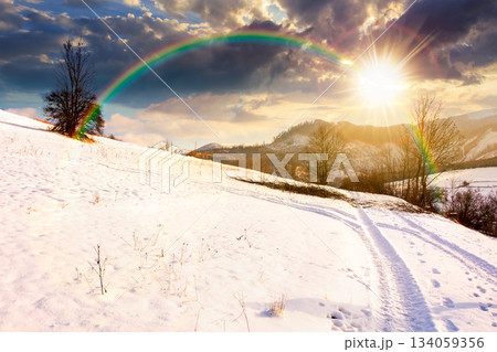 winter landscape with snow covered forested hills at sunset. mountains in cold weather in evening light. rural scene. christmas holiday in alpine region. storytelling cinematic image under the rainbow 134059356