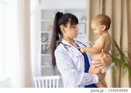 Pediatrician holding smiling infant baby during checkup in clinic Pediatrician holding smiling infant baby during checkup in clinic 134059898