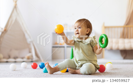 Smiling baby sitting on floor holding colorful ball and ring toy Smiling baby sitting on floor holding colorful ball and ring toy 134059927