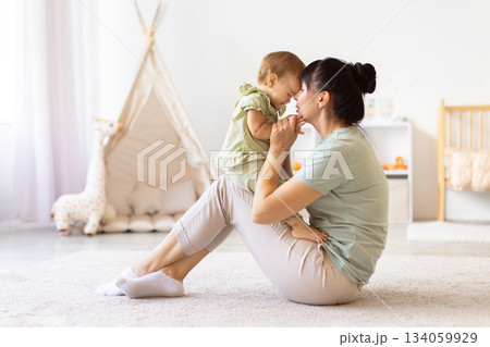 Mother sitting on floor holding her baby close as they touch foreheads Mother sitting on floor holding her baby close as they touch foreheads 134059929