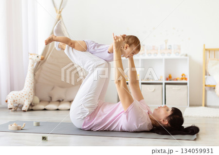 Mother lifting baby above her legs during playful exercise on yoga mat Mother lifting baby above her legs during playful exercise on yoga mat 134059931