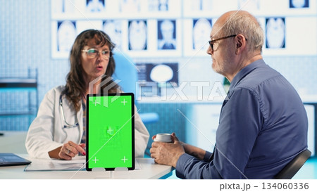 Senior man patient arriving at appointment with physician next to mockup, sharing his fears and pains for wellness. Old general practitioner offering medical advice, healthcare provider. Camera B. 134060336