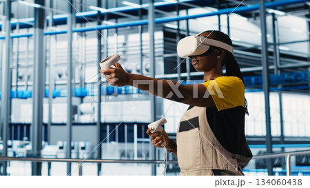 Smart factory engineer implements automated workflows and control systems using virtual reality, computerizing operations. Technician integrates sensors into production using VR headset, camera A 134060438