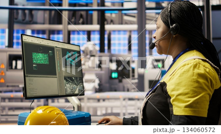 Call center agent in smart factory using headset to assist remotely with maintenance queries, monitoring automated solar panel assembly processes, providing technical guidance, camera A Call center agent in smart factory using headset to assist remotely with maintenance queries, monitoring automated solar panel assembly processes, providing technical guidance, camera A 134060572