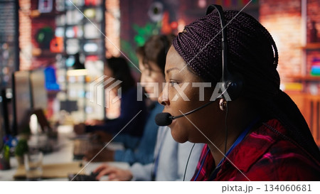Employee talking with customer using headphones microphone to identify new sales opportunities. Account manager in office using audio headset, bonding with client to generate leads, camera B close up Employee talking with customer using headphones microphone to identify new sales opportunities. Account manager in office using audio headset, bonding with client to generate leads, camera B close up 134060681