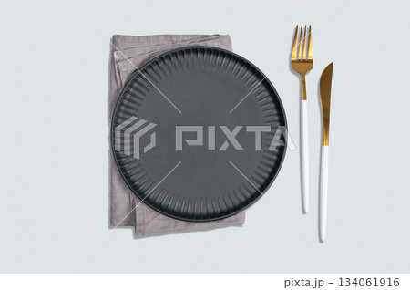 A black textured plate with a fork, knife, and linen napkin on a light background. A black textured plate with a fork, knife, and linen napkin on a light background. 134061916