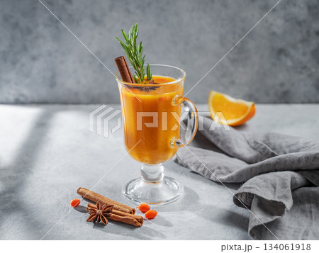 Sea buckthorn herbal tea in a glass on a blue background with orange, spices, and shadow. Sea buckthorn herbal tea in a glass on a blue background with orange, spices, and shadow. 134061918