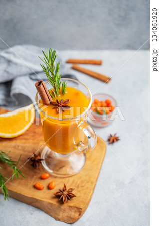 Sea buckthorn herbal tea in a glass on a wooden board on a blue background with orange Sea buckthorn herbal tea in a glass on a wooden board on a blue background with orange 134061920