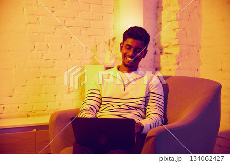 Smiling man using laptop while relaxing in warm cozy room 134062427