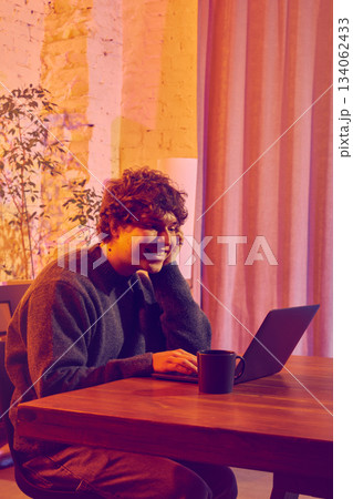 Man working on laptop and drinking coffee in warm evening office. Man working on laptop and drinking coffee in warm evening office. 134062433