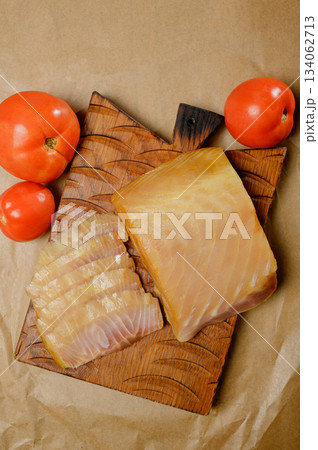 Sliced smoked or dried fish fillet on a wooden board with tomatoes Sliced smoked or dried fish fillet on a wooden board with tomatoes 134062713
