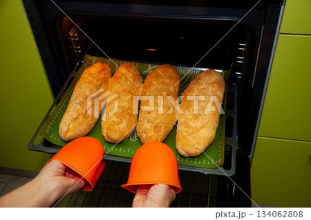 Homemade bread on a baking sheet is taken out of the oven. Long loaf, baguette at home in the kitchen. Bakery products. Cook at home. Homemade bread on a baking sheet is taken out of the oven. Long loaf, baguette at home in the kitchen. Bakery products. Cook at home. 134062808