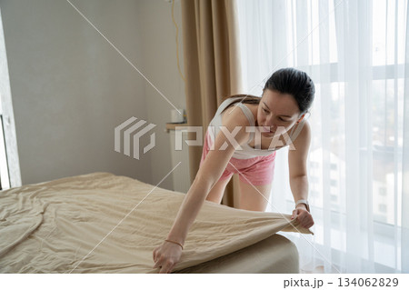 A caucasian 30-year-old woman made her bed in her bedroom on a sunny day. morning routine 134062829