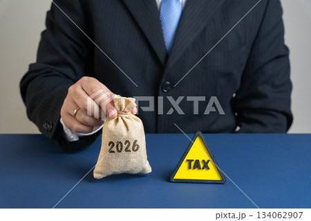 Upcoming tax policies, financial planning, fiscal regulations, corporate taxation. Tax deadlines, government levies, financial obligations. A man holds a money bag 2026 near a sign with the word tax. 134062907