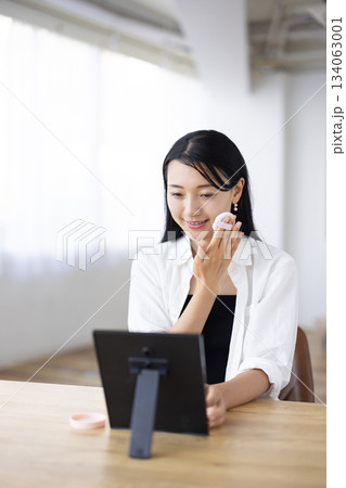 窓辺のテーブルで鏡を見ながらパフを使って化粧をする女性 窓辺のテーブルで鏡を見ながらパフを使って化粧をする女性 134063001