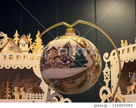 Hand painted Christmas bauble showing snowy village scene on golden holder. Nostalgic winter mood, handmade craft, peaceful holiday memory, magic and emotional festive charm 134065093