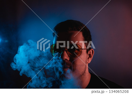 Man in neon light enjoying hookah smoke at a vibrant evening lounge atmosphere 134065208