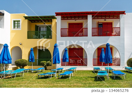Picturesque Beachfront Resort with Colorful Buildings and Relaxing Sun Loungers, Greece 134065276