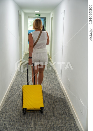 Woman with Yellow Luggage Walking Down Hotel Hallway on Vacation, Tourism and Travel Concept 134065300