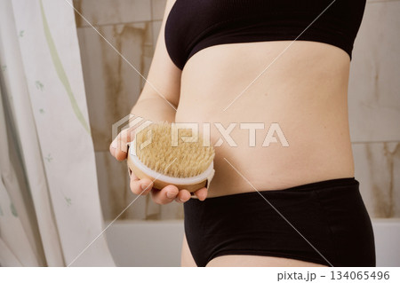 Woman performing dry brushing for skin exfoliation and wellness in bathroom 134065496
