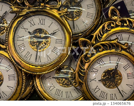 Golden vintage-style clock ornaments stacked in festive display. New Year symbolism, countdown moment, nostalgic Christmas decor and elegant holiday tradition mood Golden vintage-style clock ornaments stacked in festive display. New Year symbolism, countdown moment, nostalgic Christmas decor and elegant holiday tradition mood 134065676