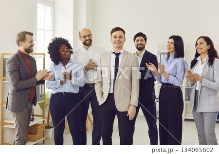 Joyful team of business professionals applauding male colleague in office space. 134065802