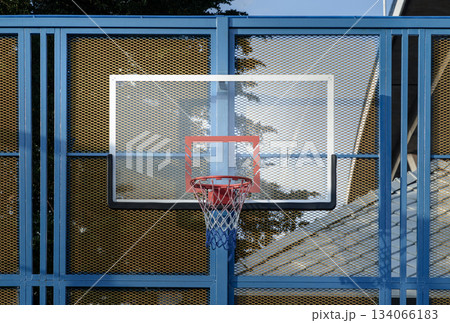 A basketball hoop, featuring an orange metal rim and net mounted on a Fiberglass Basketball Backboard. A basketball hoop, featuring an orange metal rim and net mounted on a Fiberglass Basketball Backboard. 134066183