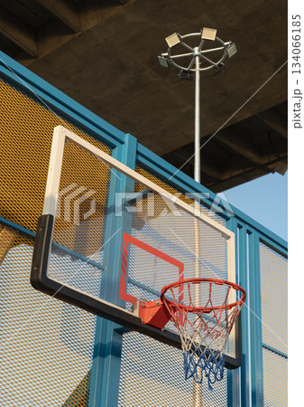 A low-angle view captures a basketball hoop with an orange metal rim and net, mounted on a fiberglass basketball backboard. A low-angle view captures a basketball hoop with an orange metal rim and net, mounted on a fiberglass basketball backboard. 134066185