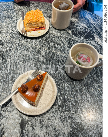 Coffee shop dessert moment with cake and tea. Flat lay of cheesecake slice and steaming cup of tea. Image for food blogging, cafe reviews, and social media content. Vertical 134066254