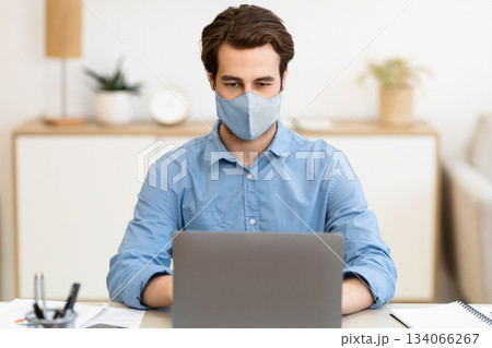 Businessman Wearing Face Mask Working On Laptop Computer Online Sitting At Workplace In Modern Office. Remote Work, Business And Entrepreneurship During Coronavirus Pandemic Concept Businessman Wearing Face Mask Working On Laptop Computer Online Sitting At Workplace In Modern Office. Remote Work, Business And Entrepreneurship During Coronavirus Pandemic Concept 134066267