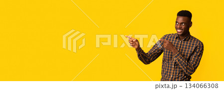 Look There. Cheerful African American Guy Pointing Aside At Copy Space Over Yellow Background With Two Fingers, Positive Black Male Showing Free Place For Your Design Or Advertisement, Panorama Look There. Cheerful African American Guy Pointing Aside At Copy Space Over Yellow Background With Two Fingers, Positive Black Male Showing Free Place For Your Design Or Advertisement, Panorama 134066308